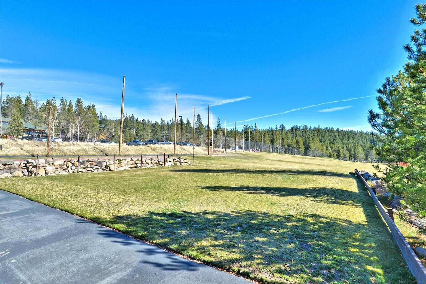 A clear, sunny day at a park with a paved path, grassy areas, and a stone wall.