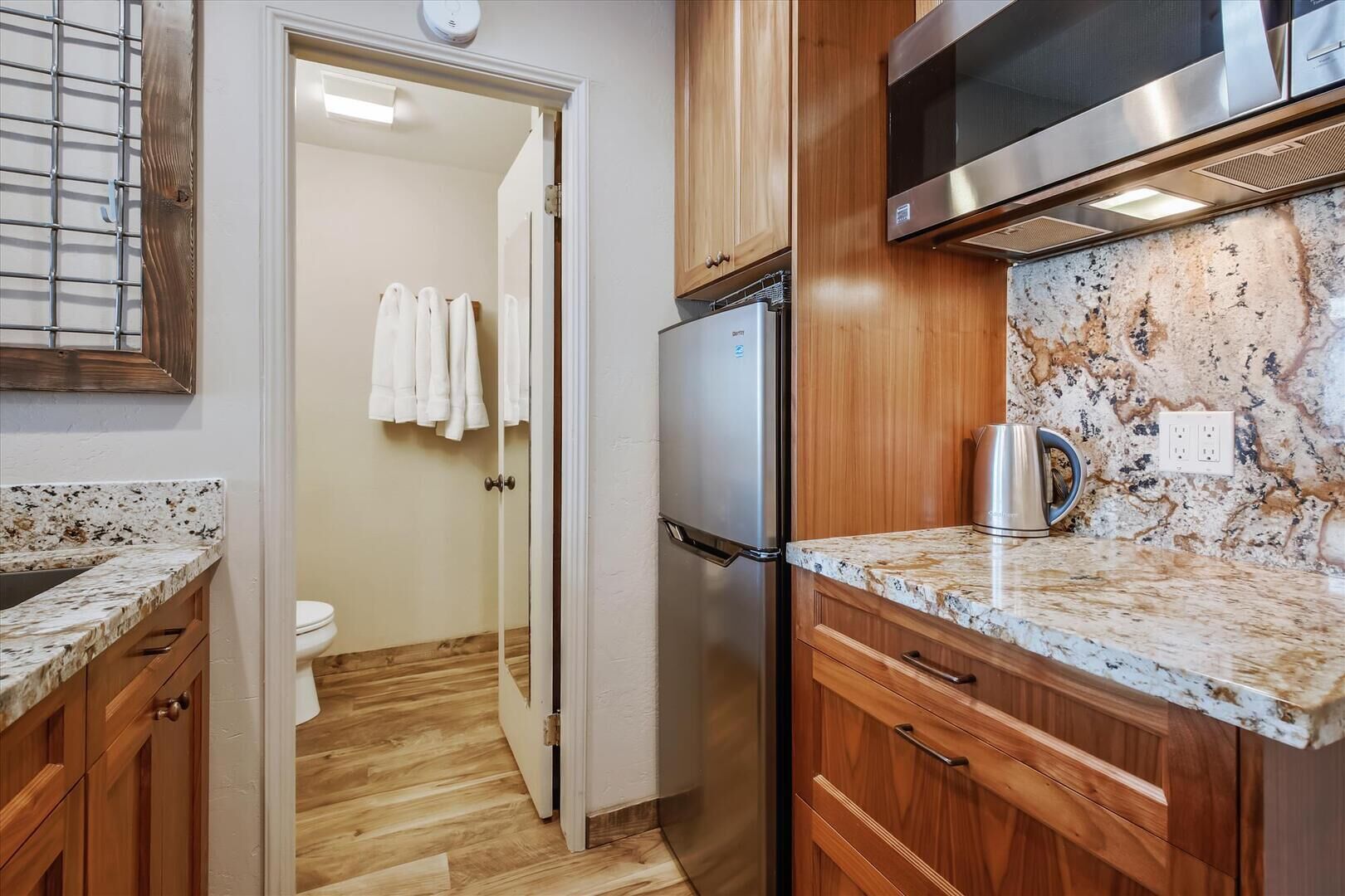 A kitchen with wooden cabinets, a stainless steel refrigerator, granite countertops, and a coffee maker.