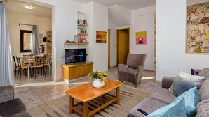 Un salon comprenant une table basse en bois, un canapé, un téléviseur, une bibliothèque et un coin repas avec des chaises et une table.