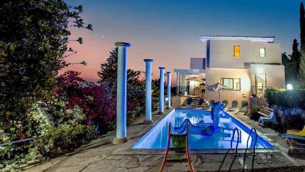 Une piscine entourée d’une végétation luxuriante, avec une maison moderne en arrière-plan.