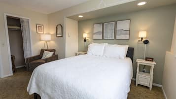 A neatly made bed in a hotel room with a closet, two bedside lamps, and framed artwork on the wall.