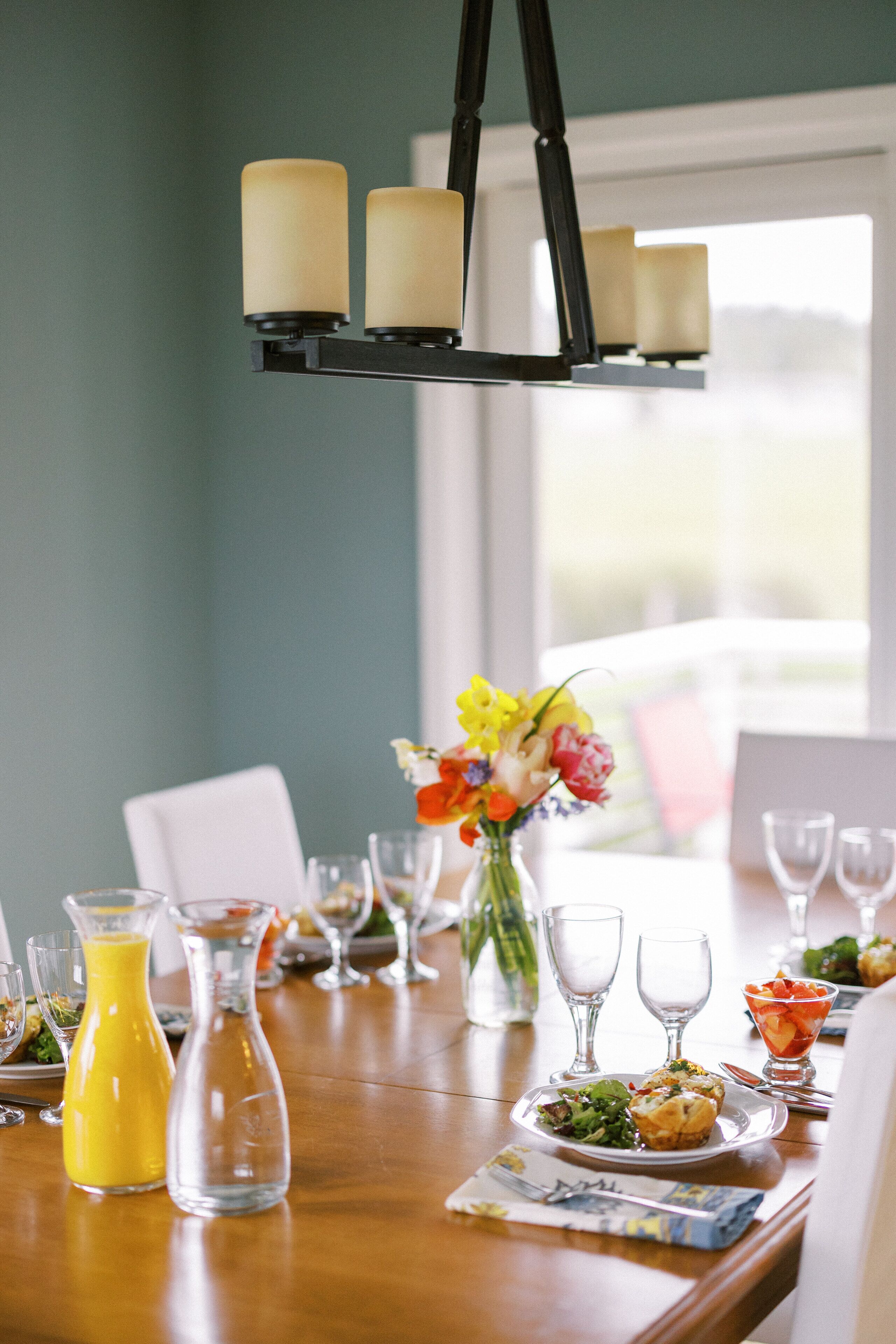 Una mesa de comedor dispuesta con diferentes platos, vasos y un jarrón de flores.