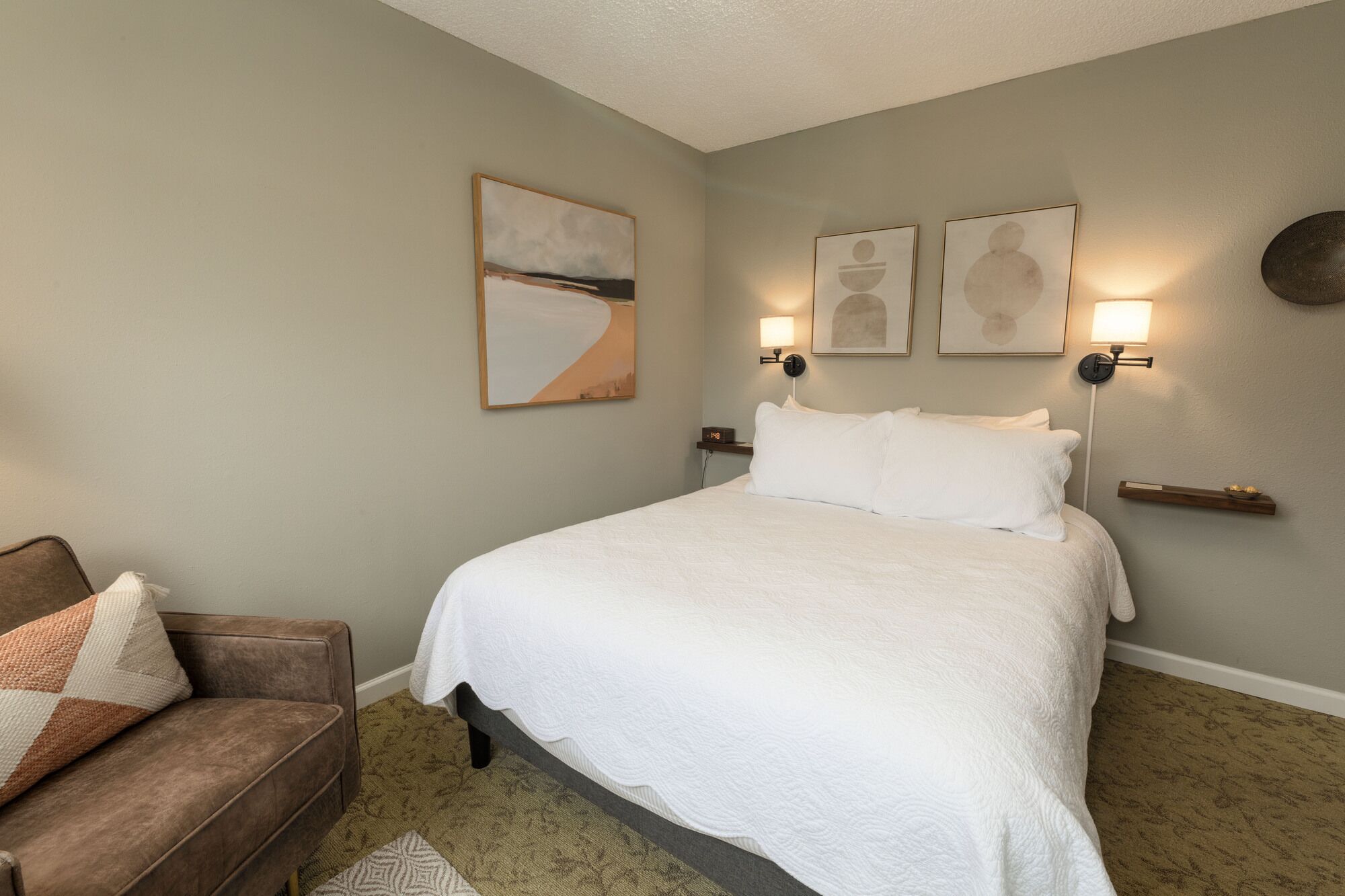 A neatly arranged bedroom with a large bed, a brown couch, and wall-mounted artwork.