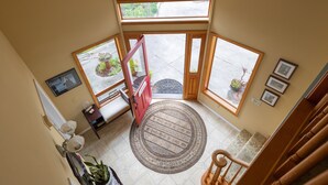 A spacious entryway with a wooden staircase, a patterned rug, and potted plants.