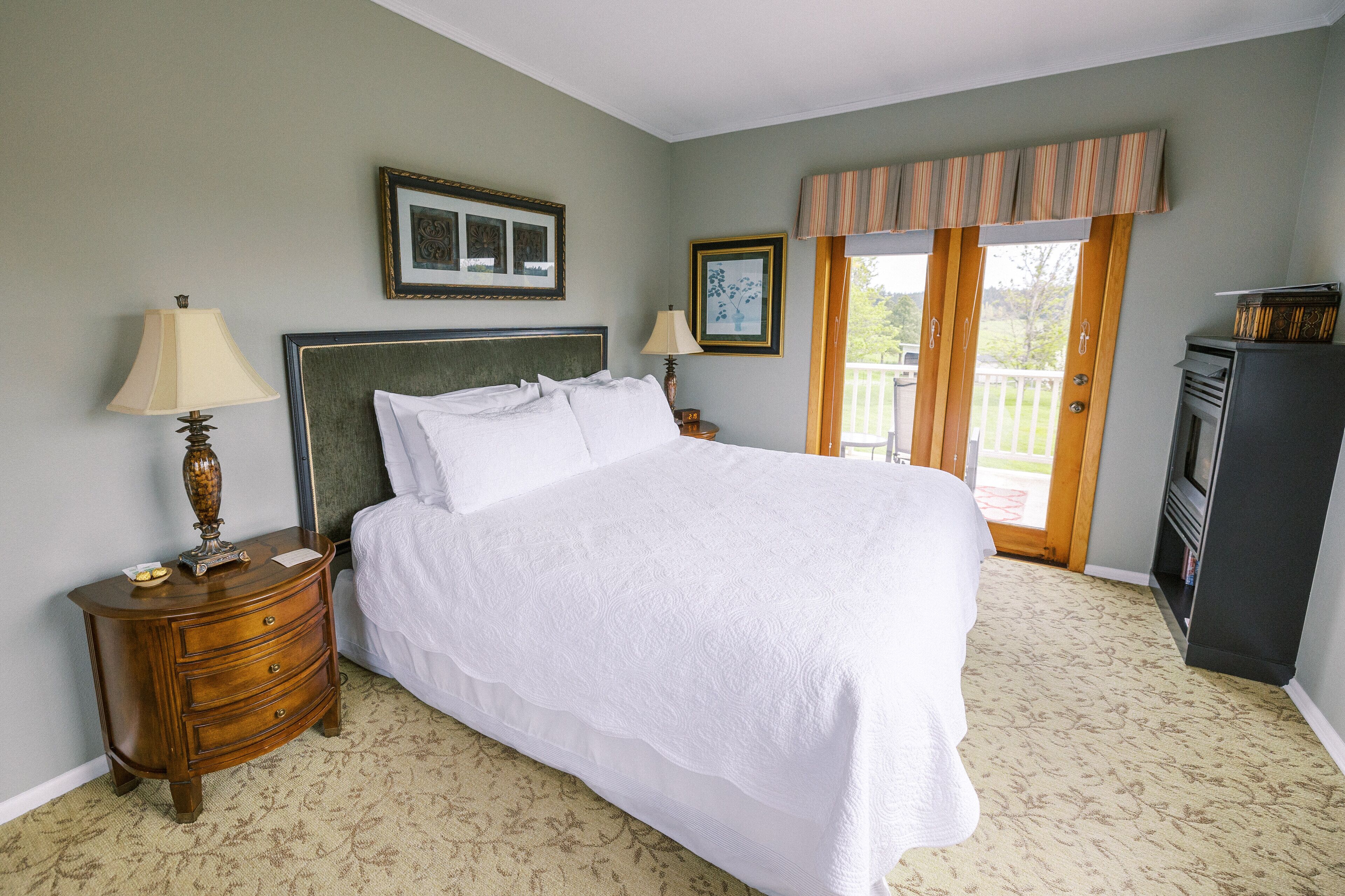 A bedroom with a large bed, two bedside tables with lamps, a dresser, a television, and a balcony with a view.