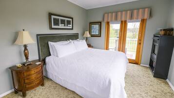 A bedroom with a large bed, two bedside tables with lamps, a dresser, a television, and a balcony with a view.