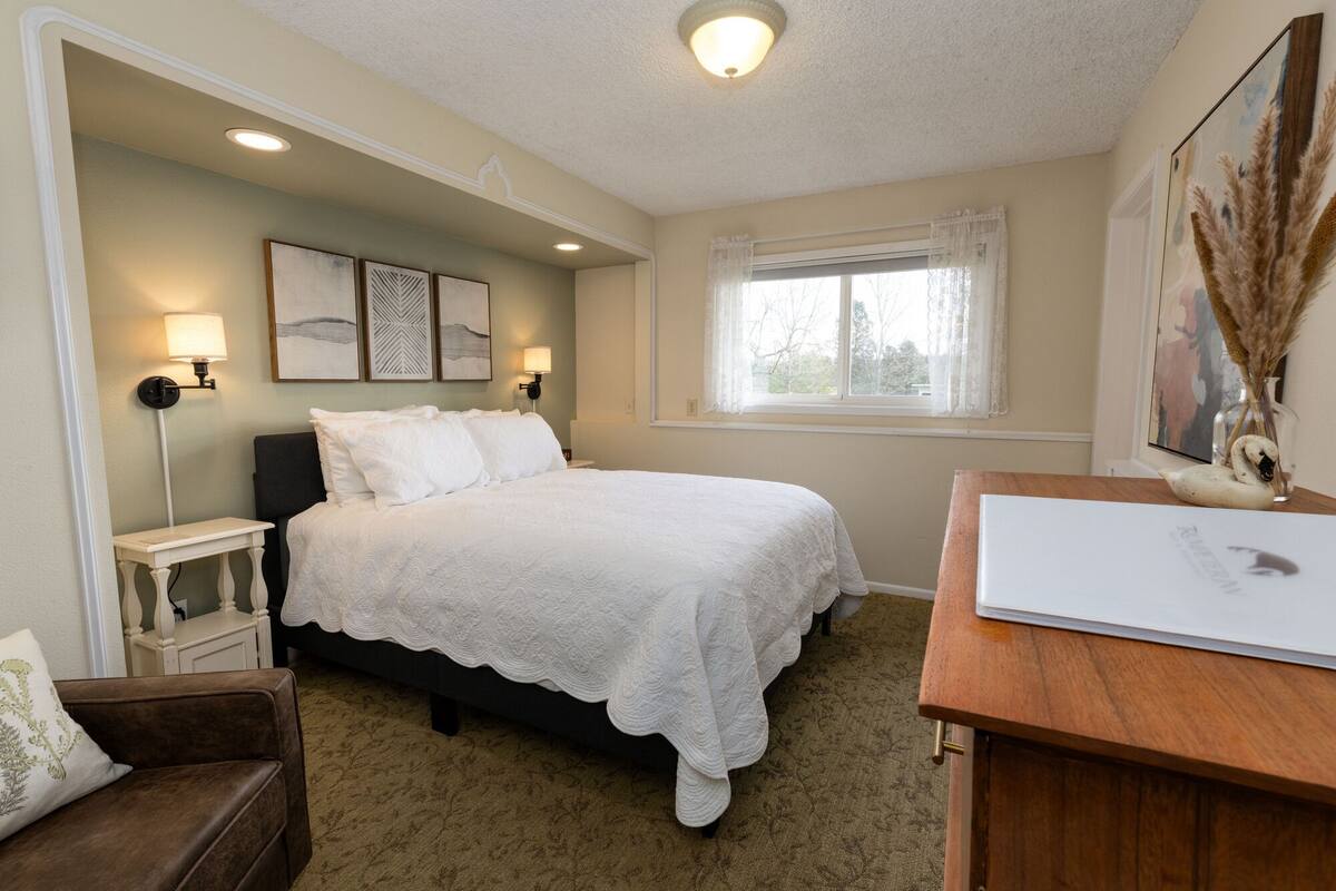 A bedroom with a bed, bedside tables, a desk, and a window.