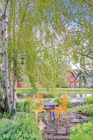 A serene outdoor seating area with a table and chairs, surrounded by lush greenery and a tree.