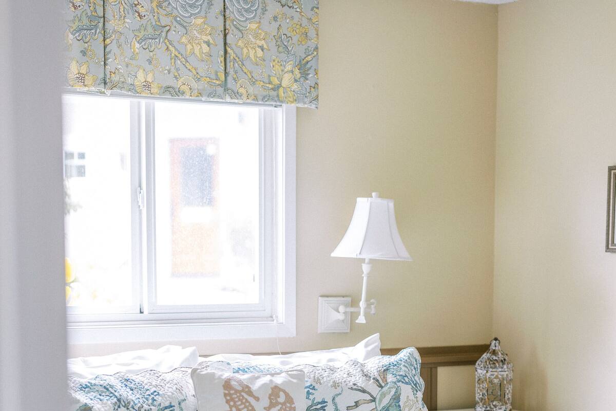 A bedroom with a bed, a nightstand, a lamp, and a window with curtains.