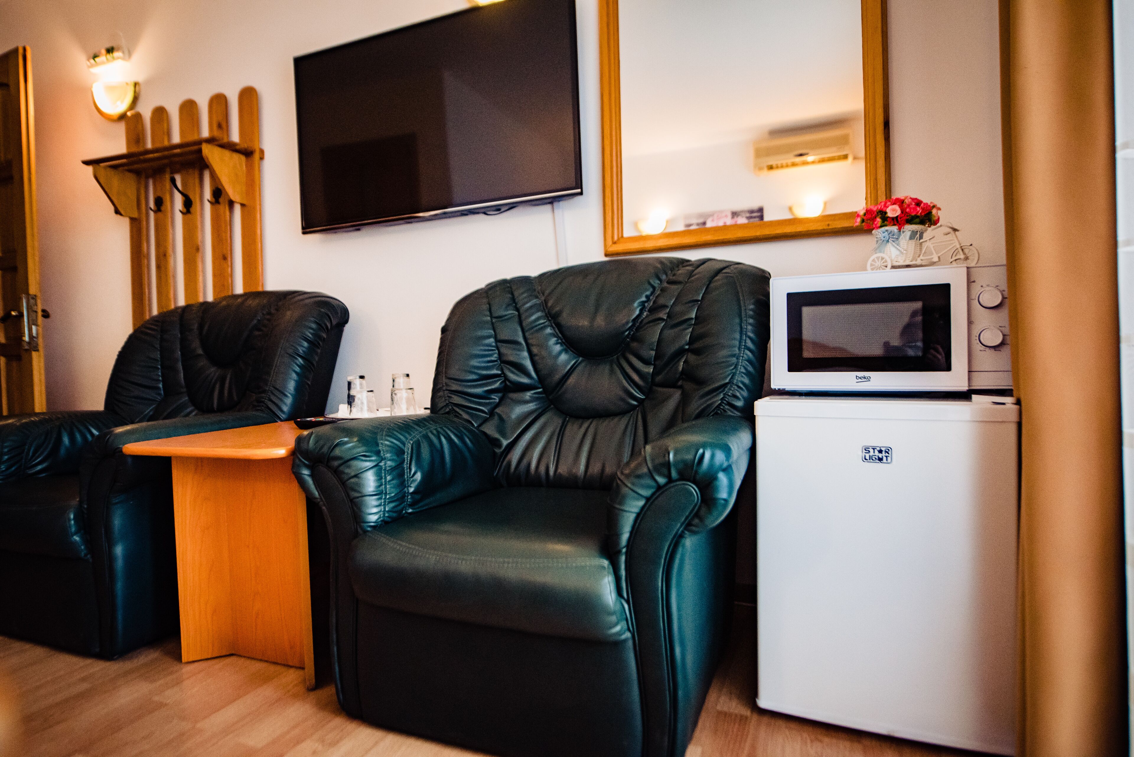 Une pièce comprenant deux fauteuils en cuir, une petite table en bois, un four à micro-ondes et un téléviseur fixé au mur.