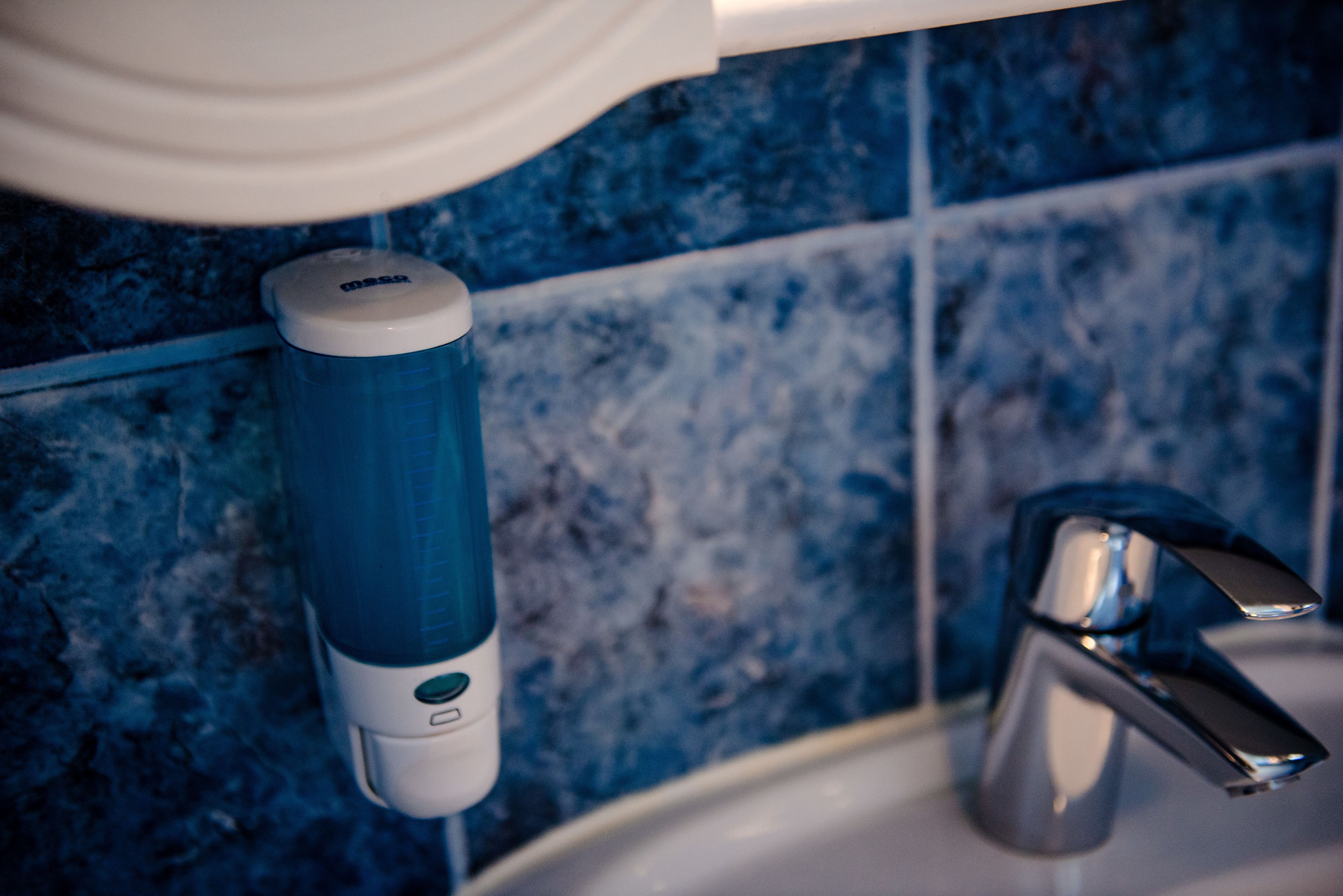 A bathroom with blue tiles, a white soap dispenser, and a chrome faucet.