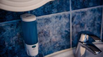 A bathroom with blue tiles, a white soap dispenser, and a chrome faucet.