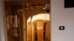 A hotel elevator with a mirrored interior and a wooden door leading to a lobby with a leather sofa. - Pensiune Roua (Arad)