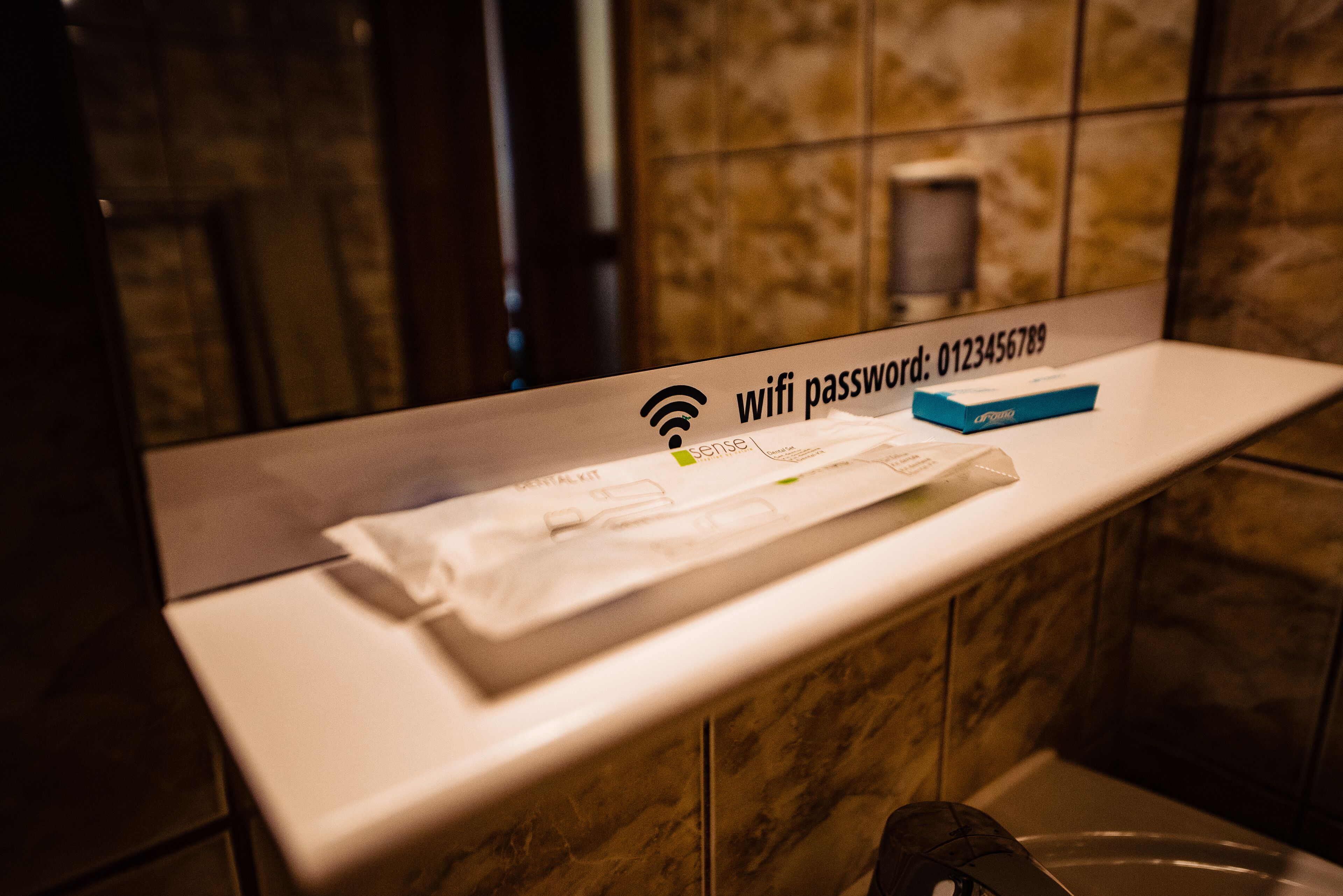 A bathroom with a towel rack, a sign indicating a wifi password, and a blue box on the counter.