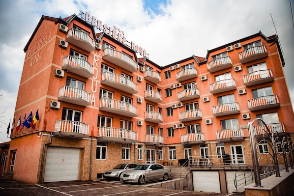 Een meerlaags hotel met balkons, airconditioners en een parkeerplaats met auto's.