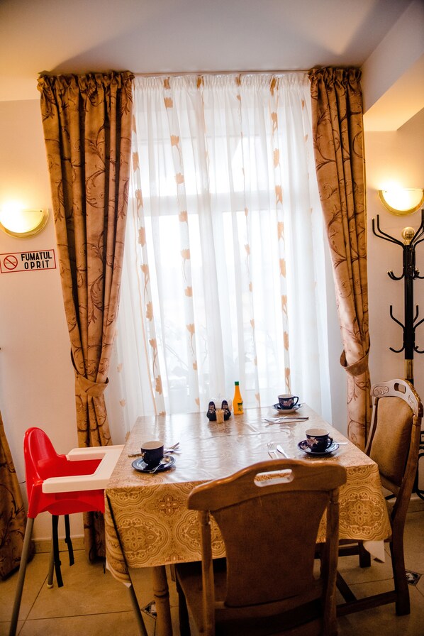 Un comedor con una mesa dispuesta para dos, una silla roja, una silla marrón y un perchero en la pared.