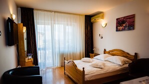 A hotel room with a wooden bed, a desk, a chair, a television, and a window with curtains. - Pensiune Roua (Arad)