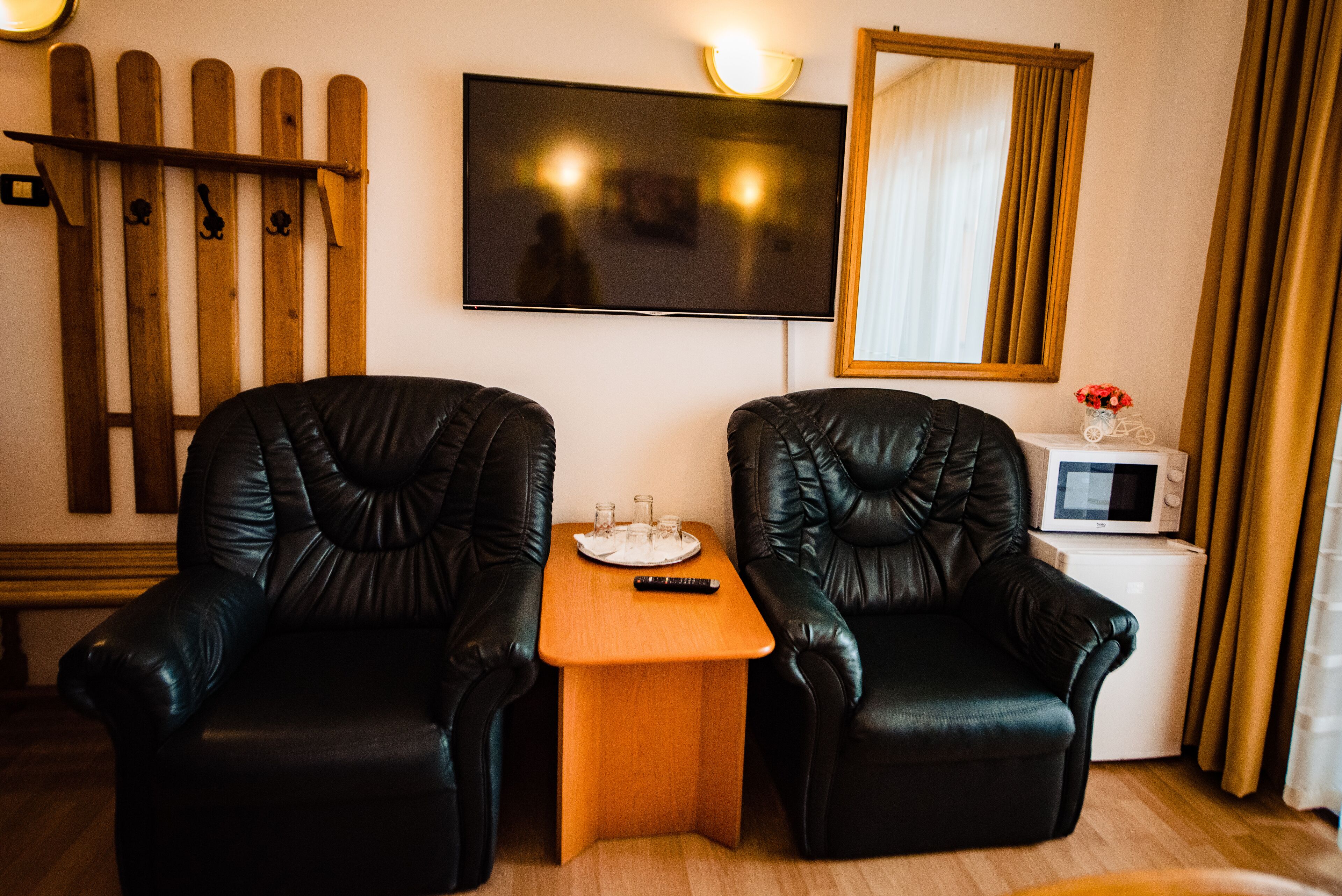 Una habitación con dos sillones de cuero negro, una mesa de madera con un control remoto, un televisor, un refrigerador blanco pequeño y una valla de madera contra la pared.