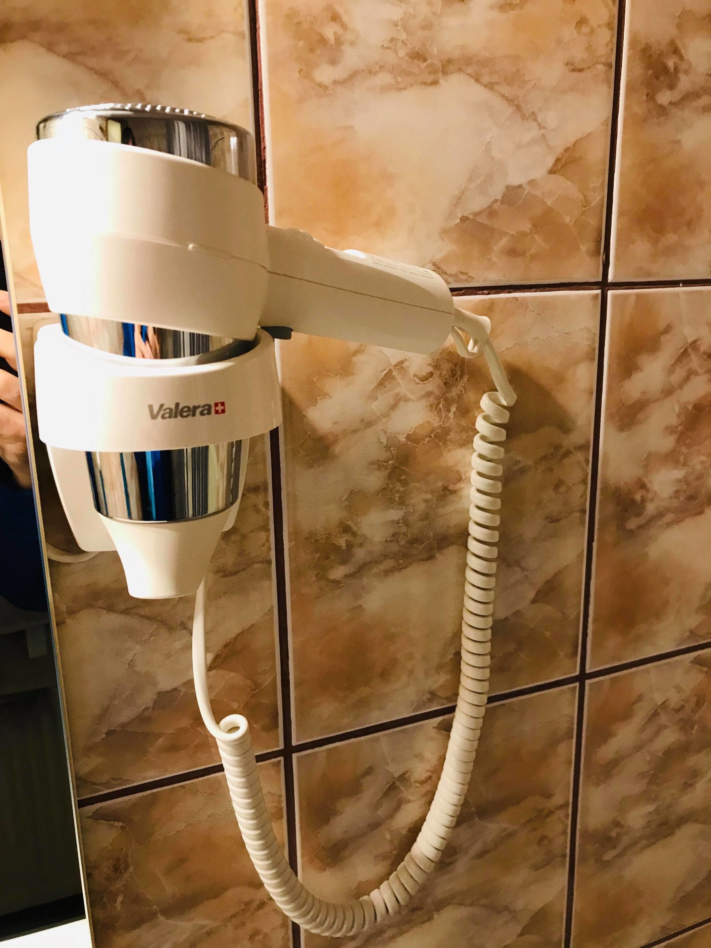 Un secador de pelo con cable, fijado a una pared de azulejos.