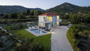 Una casa de dos pisos con piscina, rodeada de vegetación y colinas.