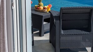 Una mesa de mimbre con una cesta de fruta y un vaso de zumo de naranja junto a una piscina.