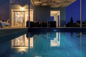 Un espace piscine moderne avec une eau cristalline, un coin salon avec des sièges et une grande fenêtre donnant sur la piscine.