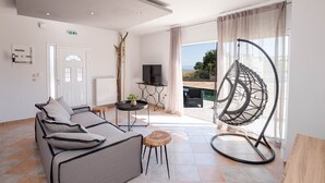 Una sala moderna con sofá, sillón colgante, televisor y vista a una piscina.