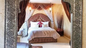 A bedroom with a large ornate mirror, a bed with patterned bedding, and a potted plant.