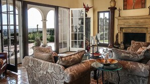 A spacious living room with a fireplace, comfortable seating, and a view through large glass doors to an outdoor area.