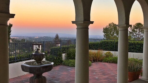 An outdoor patio with a fountain, arches, and a view of the cityscape at sunset.