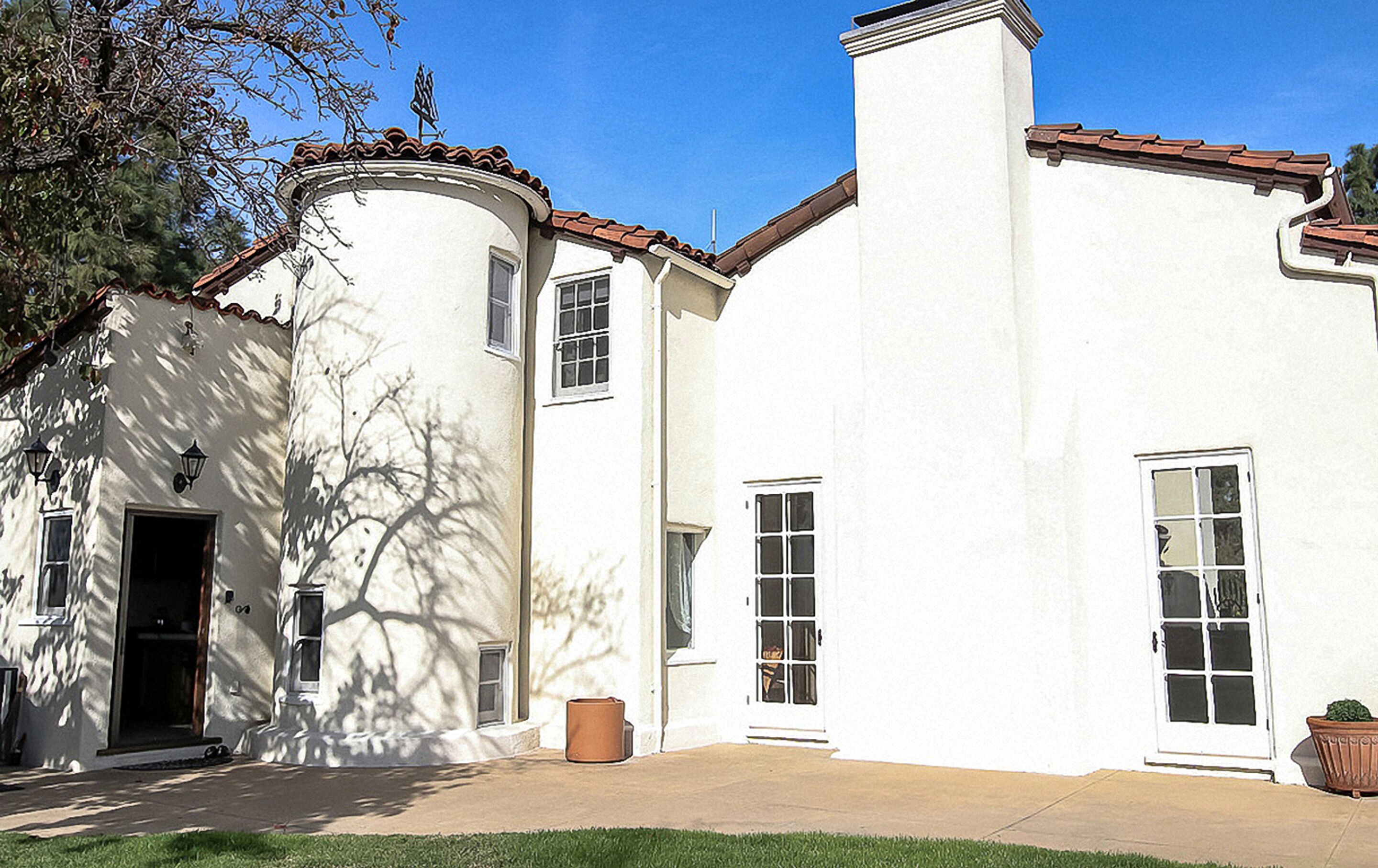 A two-story building with a white exterior, a brown roof, and a chimney. There are two windows on the ground floor and two on the upper floor.