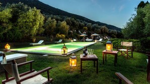 Un espace piscine avec des chaises longues, une table à manger avec des verres et des bouteilles, et des lanternes.