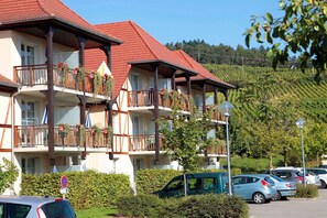 A multi-story building with balconies, a parking area, and a hilly landscape in the background. - Apartment in Bergheim near Picturesque Town (Bergheim)