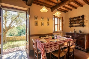 Un coin repas avec une table dressée pour quatre personnes, des chaises en bois, une nappe à carreaux rouges et blancs, et une vue sur les arbres à travers une porte vitrée.