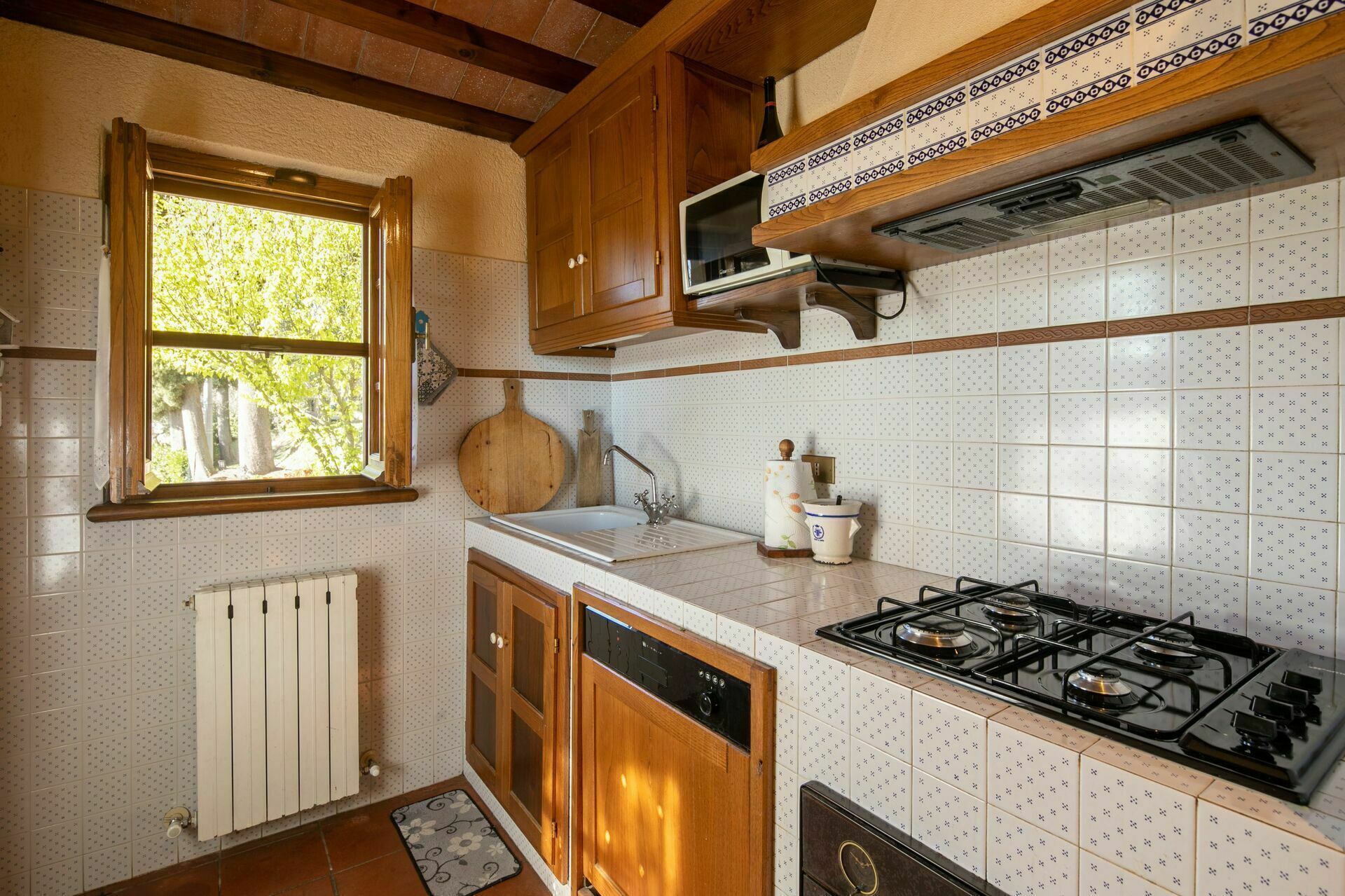 A kitchen with wooden cabinets, a gas stove, a microwave, and a window with a view of trees.