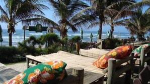Eine Holzterrasse mit Sitzgelegenheiten im Freien, Palmen und Blick auf das Meer.