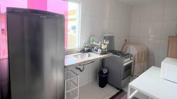 Uma cozinha compacta com azulejos brancos, geladeira, pia, fogão e micro-ondas.