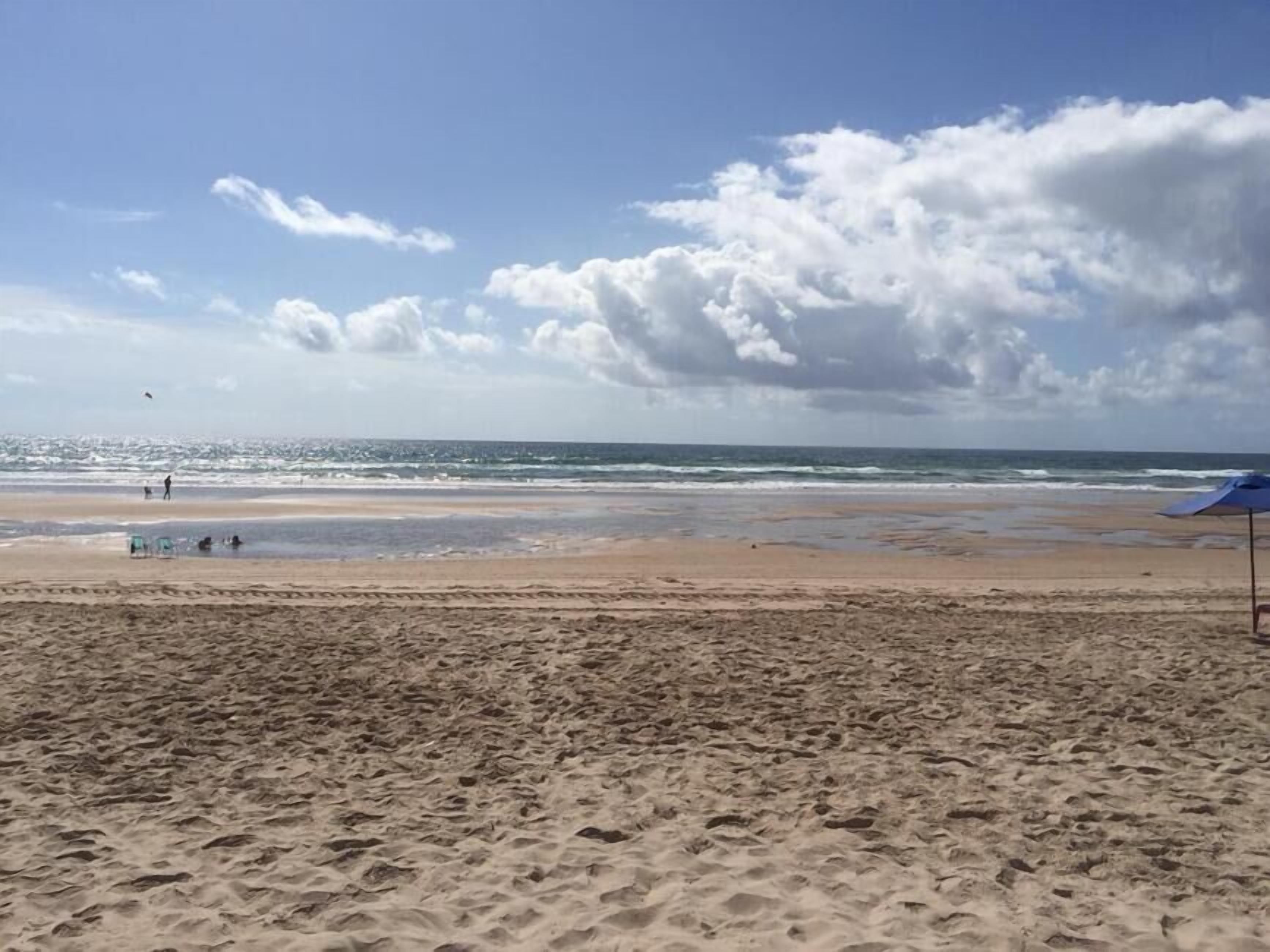 A beach with a sandy foreground and a clear view of the ocean.