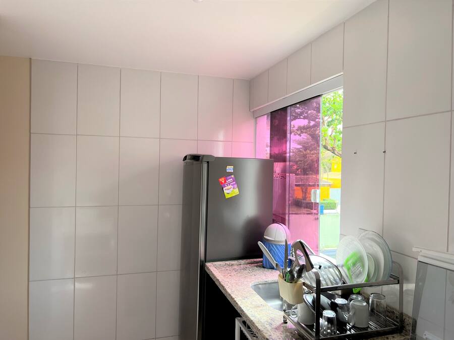 Una cocina con baldosas blancas, un refrigerador de acero inoxidable, un escurreplatos y un ventanal con vistas a zonas verdes.
