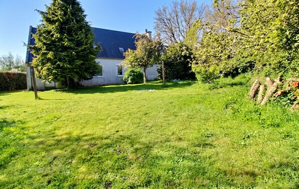 A house with a sloped roof, a well-maintained lawn, and a variety of trees and shrubs.
