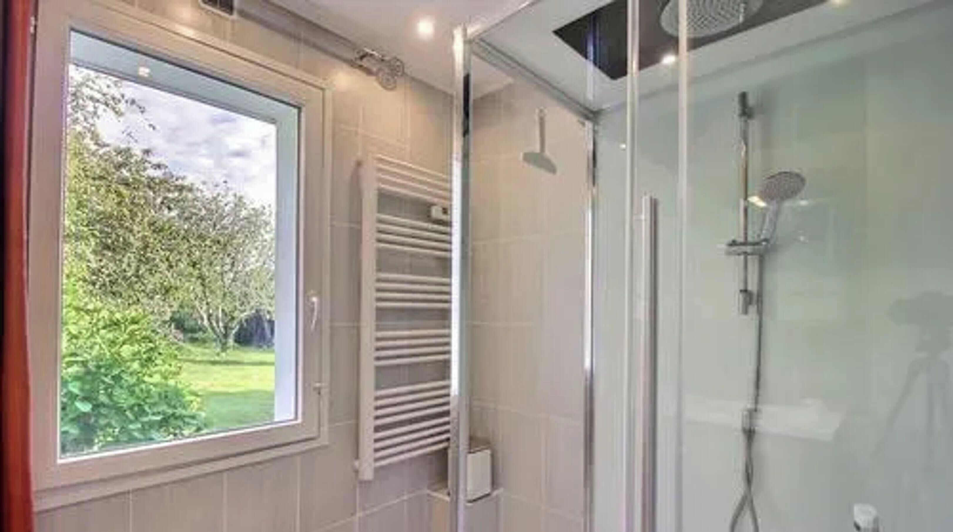 A bathroom with a glass shower enclosure, a window with a view of greenery, and a towel rack.
