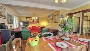 A dining area with a wooden table set for four, a television, and a red sofa in the background.