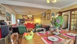 A dining area with a wooden table set for four, a television, and a red sofa in the background.