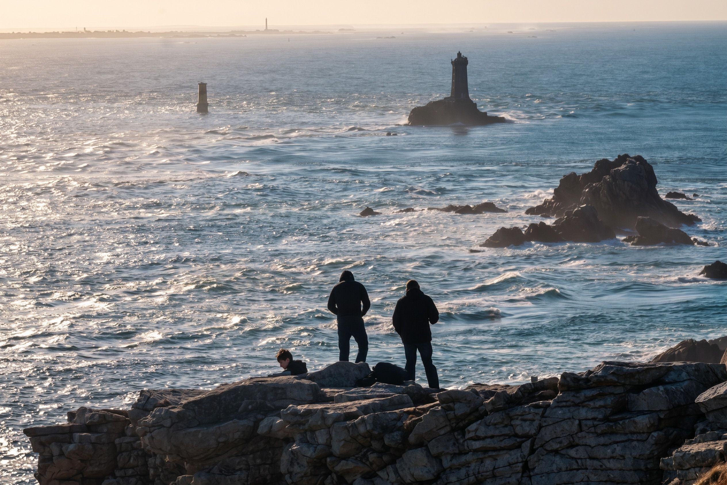 Un paysage côtier avec des affleurements rocheux et un phare à l’horizon.