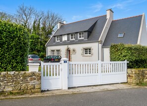 A two-story house with a stone wall and a white gate.
