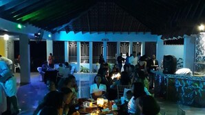 A group of people seated around a table with candles, under a covered area with a patterned ceiling. - El Currican (Guayacanes)
