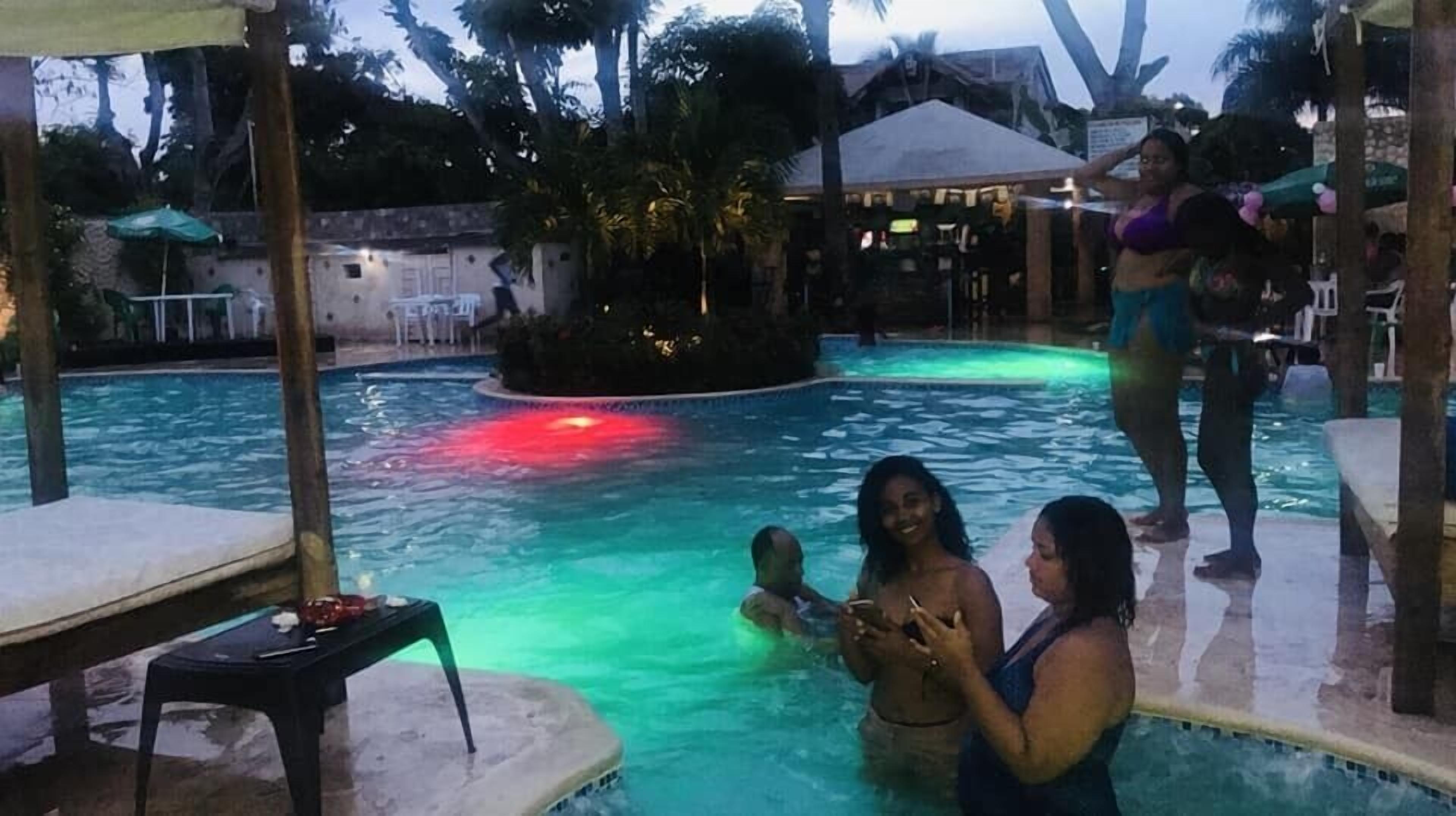 Una piscina con luces rojas, rodeada de sillas de descanso y sombrillas.