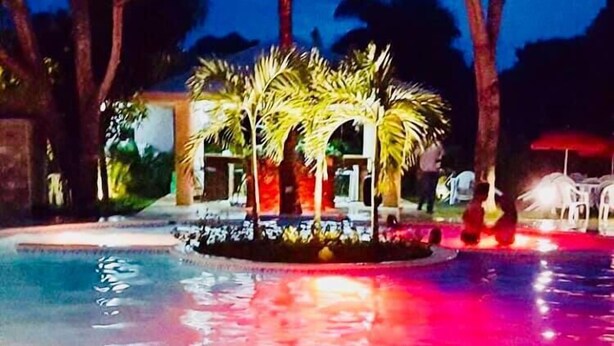 A swimming pool with a water feature and palm trees, surrounded by a building with a red roof. - El Currican (Guayacanes)