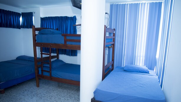 A dormitory room with bunk beds, a white pillar, and a window with blue curtains. - Hosteria la Costanera (Salinas)