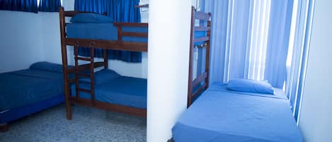 Un dormitorio con literas, un pilar blanco y una ventana con cortinas azules.